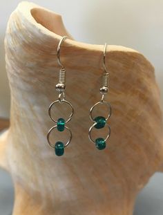 a pair of green glass beaded earrings on top of a wooden stand next to a shell