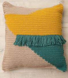 a crocheted pillow with tassels on the front and side, sitting on a wooden surface