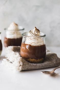 two desserts in small glass jars with whipped cream and chocolate sauce on top, sitting next to each other