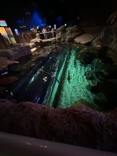 people are swimming in an artificial pool at night time with lights shining on the water