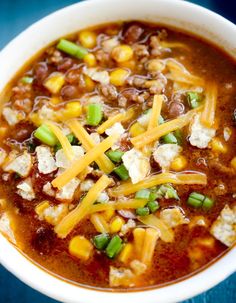 a white bowl filled with chili, beans and cheese on top of a blue table