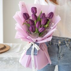 a woman holding a bouquet of purple tulips in her left hand and wearing jeans