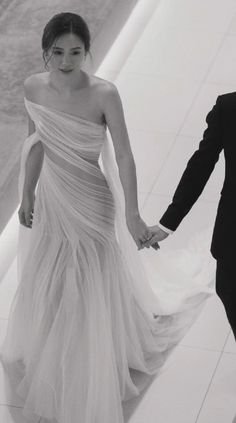 a man and woman in formal wear walking down a hall holding each other's hands