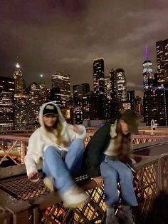 two people sitting on top of a metal railing in front of a cityscape