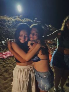 two girls hugging each other on the beach at night with their arms around one another