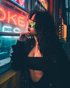 a woman standing in front of a neon sign talking on a cell phone while wearing sunglasses