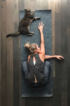 a woman laying on top of a mat with a cat sitting on her back next to her