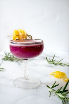 a purple drink with pineapple garnish in a glass on a white tablecloth