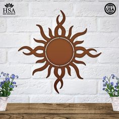 a metal sun on a white brick wall with blue flowers in the vases next to it