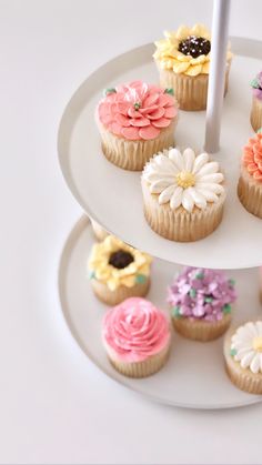 a three tiered plate holding cupcakes with flowers on them