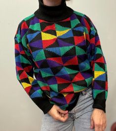 a woman wearing a multicolored sweater and jeans with her hands in her pockets