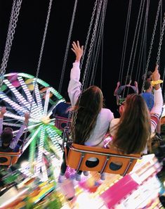 people ride on swings at an amusement park during the night time, with their hands in the air