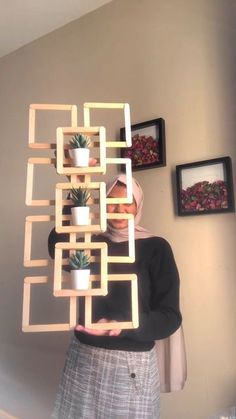 a woman standing in front of a wall holding up a planter made out of wooden blocks