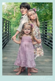 three children are standing on a wooden bridge