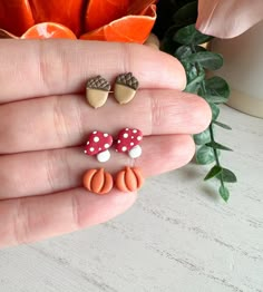 a person is holding two small earrings in their hand and there are flowers behind them