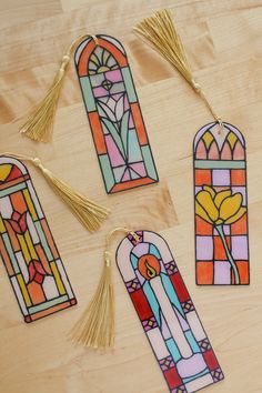 four stained glass bookmarks with gold tassels on top of a wooden table