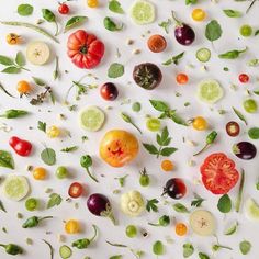 many different types of vegetables are arranged on the white surface with green leaves and tomatoes