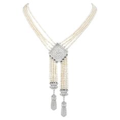 This exquisite Tassel Desing Necklace brings 1920s looks to the modern world.  A dance of cream tone 3 mm, genuine pearls, adorn the piece and the multiple strands.  An Art Deco-inspired Clasp, bow-inspired accents & center filigree pendant, are covered in diamonds, and made in solid 18K White Gold. The center of the filigree pendant has a Round cut Bezel set diamond of approximately 0.20 carats, & the rest of the diamonds in the pendant and two tassels, and its clasp are set with approx. 320 Round cut Diamonds in the metal piece, add brilliance and weigh collectively approximately 2.70 carats in total H-I  color and VS clarity Secured with an 18K Gold, diamond-accented Insert Clasp. The clasp/Pendant  measures approximately 32 mm x 32 mm, 4.5" Drop And the total length is 21.5" long. Rema Luxury White Gold Art Deco Necklace, 1920s Necklace, Pearl And Diamond Necklace, Long Pearl Necklaces, Jewelry Appraisal, Filigree Pendant, Art Deco Necklace, Tassel Jewelry, Bezel Set Diamond