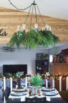 the dining room table is set with place settings for four and has greenery hanging from the chandelier