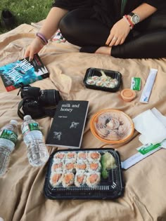 a person sitting on a blanket with food and water in front of them, including sushi