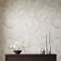 two vases with flowers on top of a wooden cabinet in front of a wallpapered background