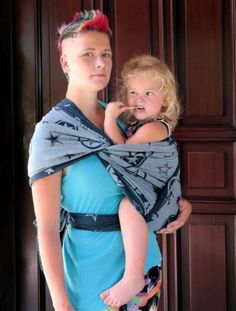 a woman holding a baby wrapped in a wrap while standing next to a wooden door