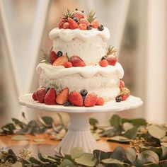 a three tiered cake with strawberries and berries on top sits on a table