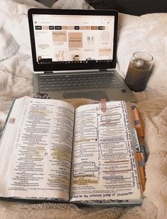 an open book sitting on top of a bed next to a laptop computer and drink