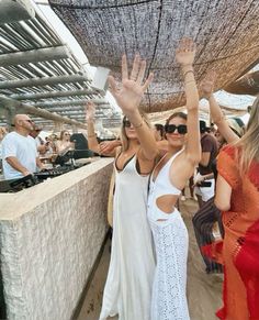 two women in white dresses standing next to each other with their hands up and arms raised