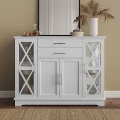 a white cabinet with glass doors and a mirror on it's top, in front of a beige wall