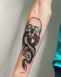 a person with a tattoo on their arm and hand is holding a snake in the shape of a skull