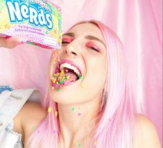 a woman with pink hair and sprinkles on her face eating a box of nerds