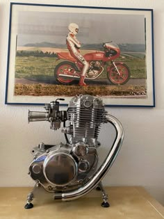 a motorcycle engine sitting on top of a wooden table in front of a painting hanging above it