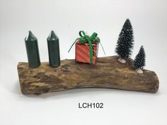 a piece of driftwood with candles and a present on it, sitting next to some small trees