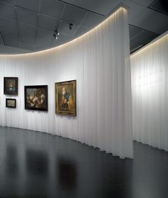 an art gallery with paintings on the wall and white drapes draped over it's walls