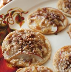 several desserts are arranged on a plate with apples and pecans in the background