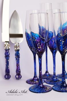 four wine glasses with blue and purple designs on them next to a knife, fork and spoon