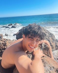 a man laying on top of a rock next to the ocean with his arms around him