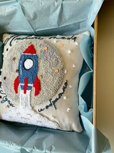 an embroidered pillow with a rocket on it in a blue gift box for someone's birthday