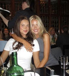 two beautiful young women sitting next to each other in front of a table with food and drinks