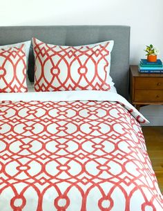 a bed with red and white pillows on top of it next to a night stand