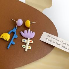 three different colored earrings on a table with a sign that says, remember when life is steep to keep your feet up