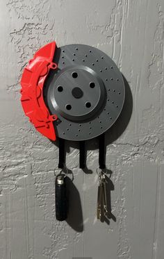 a red and black clock hanging from the side of a wall with keys attached to it