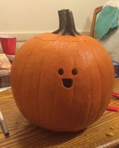 a pumpkin sitting on top of a wooden table next to a marker and pencils