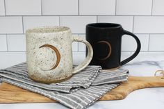 two coffee mugs sitting on top of a wooden cutting board next to each other