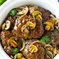 a white bowl filled with meat and mushrooms on top of a green table cloth next to vegetables