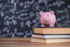 a pink piggy bank sitting on top of a stack of books in front of a chalkboard