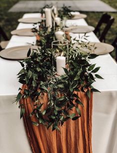 a long table with candles and greenery is set up for an outdoor dinner party