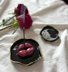 two small black plates with red lipstick on them and a single rose in the middle