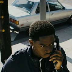 a man talking on a cell phone while standing next to a pole and parked car